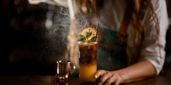 Close-up of glass with bumble coffee cocktail on the table and female bartender gently sprinkles on it