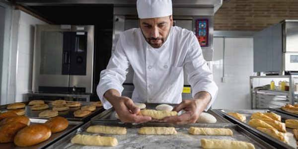 Latin American baker baking pastries at a pastry shop and putting them on a tray for the oven