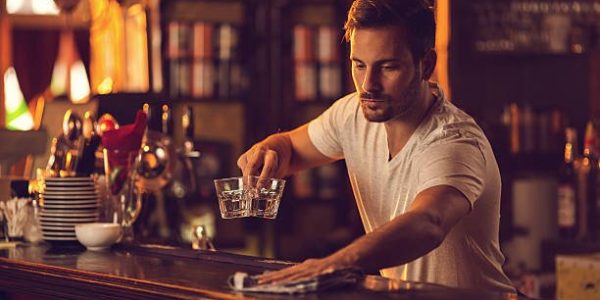 Male barista wiping and cleaning bar counter after working hours.