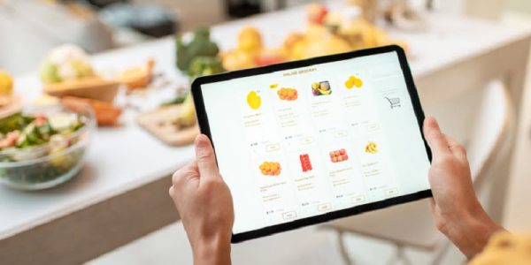 Woman shopping food online using a digital tablet at the kitchen, close-up view on a tablet screen. Concept of buying online using mobile devices